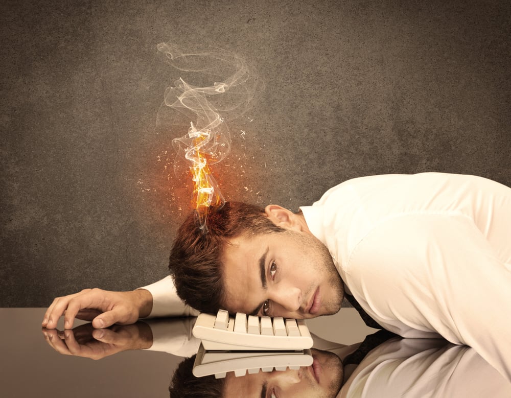 A frustrated businessman resting his head on a keyboard and shouting with his hair on smoke, catching fire