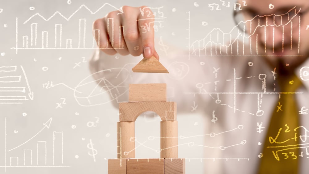 Young handsome businessman using wooden building blocks with white calculations scribbled around him